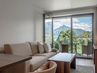 Hotelzimmer mit Sofa, Teppich, Eichenholzboden, Holzmöbeln und Balkon mit Glasgeländer